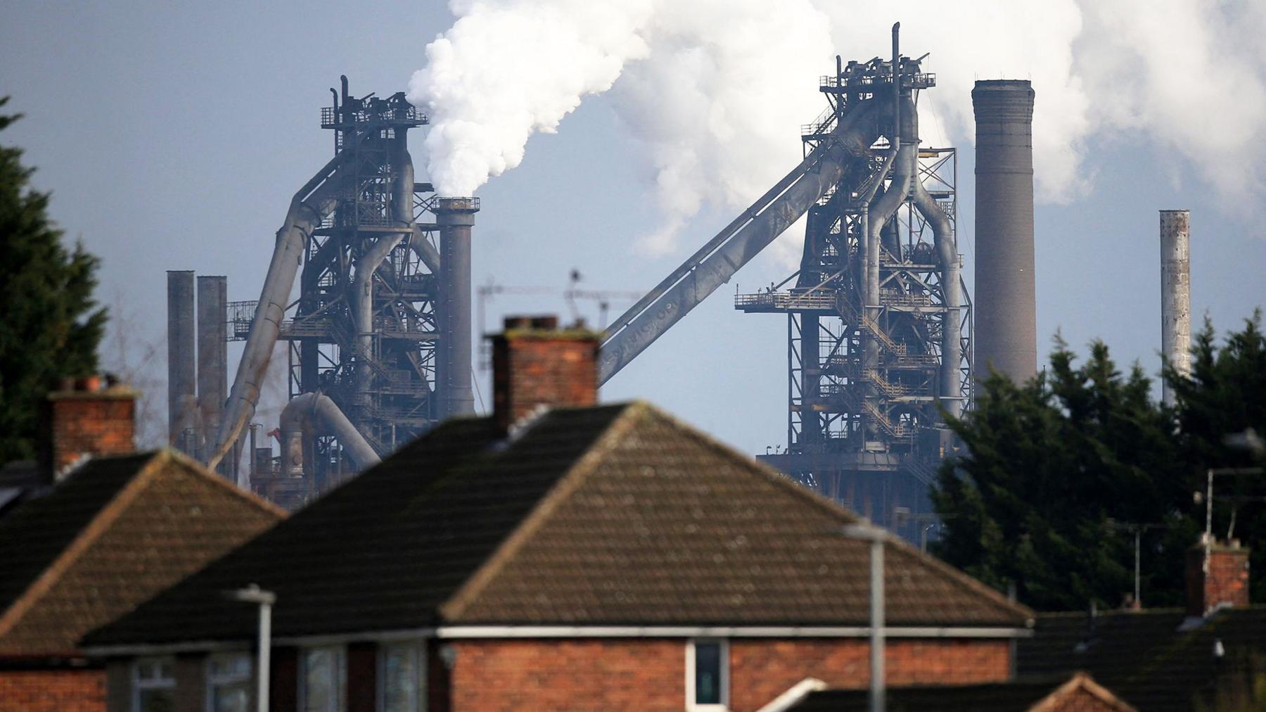 A British Steel plant, with steam billowing out of it, behind a row of terrace houses