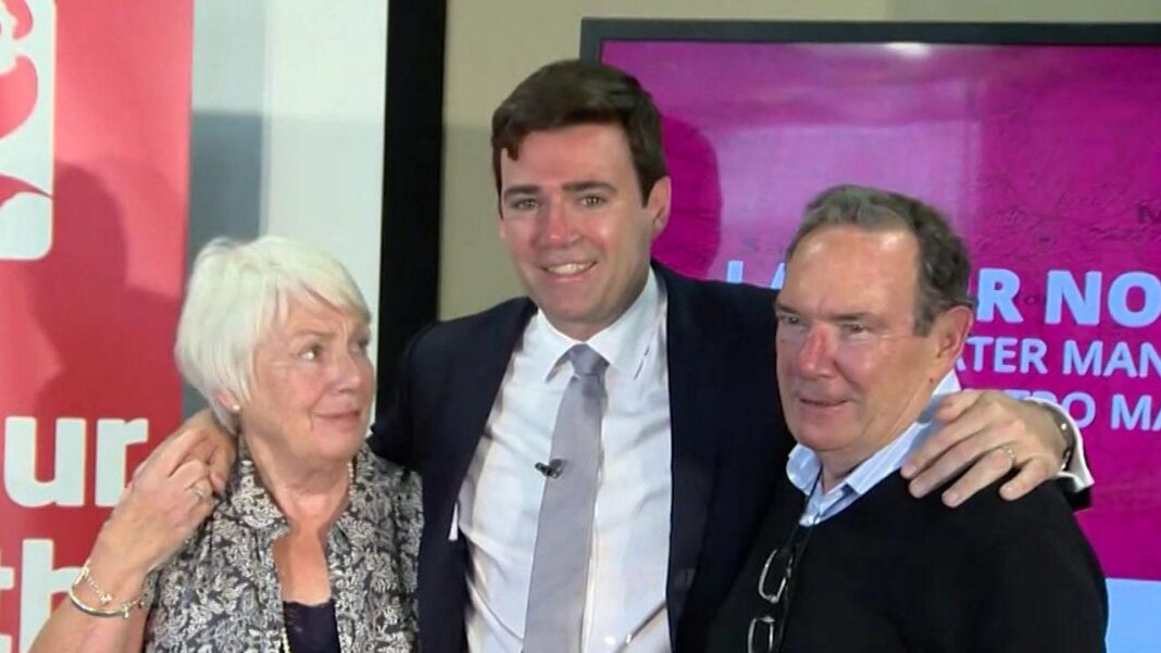 Burnham thanks well-wishers following his father’s death Head and shoulders shot of Burnham, who is smiling in between his mother and father, with his arms draped over their shoulders. He is wearing a black suit, white shirt and grey tie. His mother stands on the left with white hair and a black and white paisley shirt over a black top. His father stands o the right wearing a black jumper over a blue and white open-necked shirt.