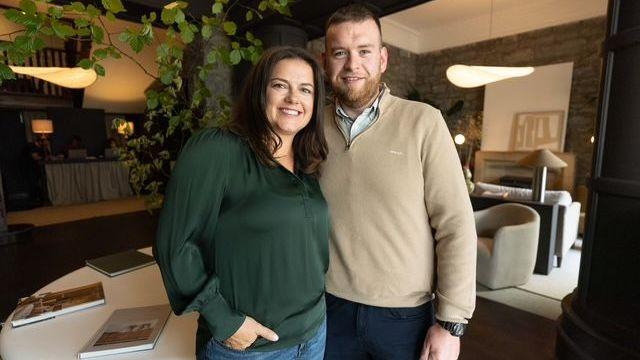 Timby's brown hair tumbles over her shoulders as she poses in a green blouse and jeans next to bearded boyfriend Jason Mangan, 38, wearing a beige cardigan, table books and manicured furniture visible in the background