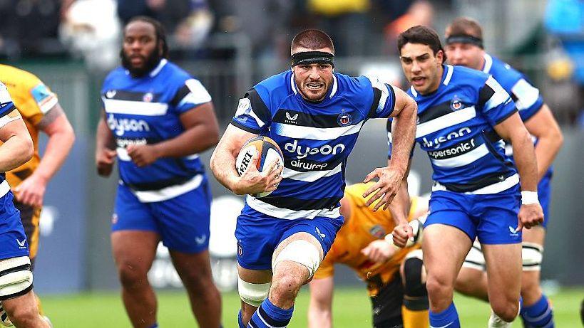 Josh Bayliss runs with the ball in his hand during a match for Bath as Santiago Carreras (right) and Beno Obano (left) stand behind watching