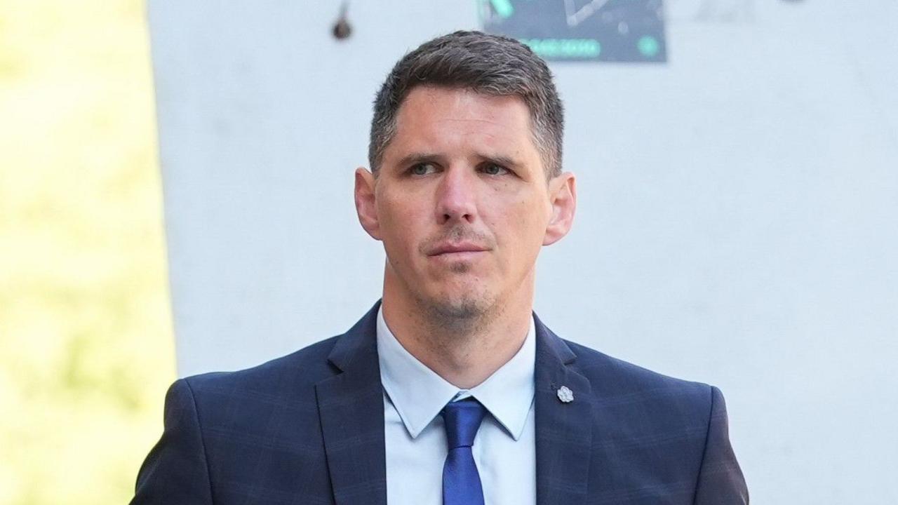 Paul Street has short brown and grey hair and is wearing a white shirt, blue tie and navy suit jacket. He is walking and looking to the left.