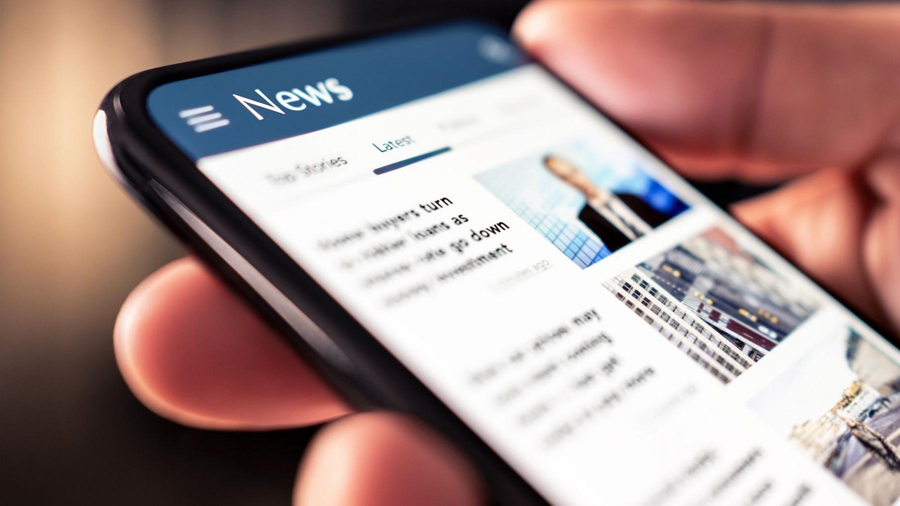 Close up oa person holding a smartphone with a generic news website on the screen