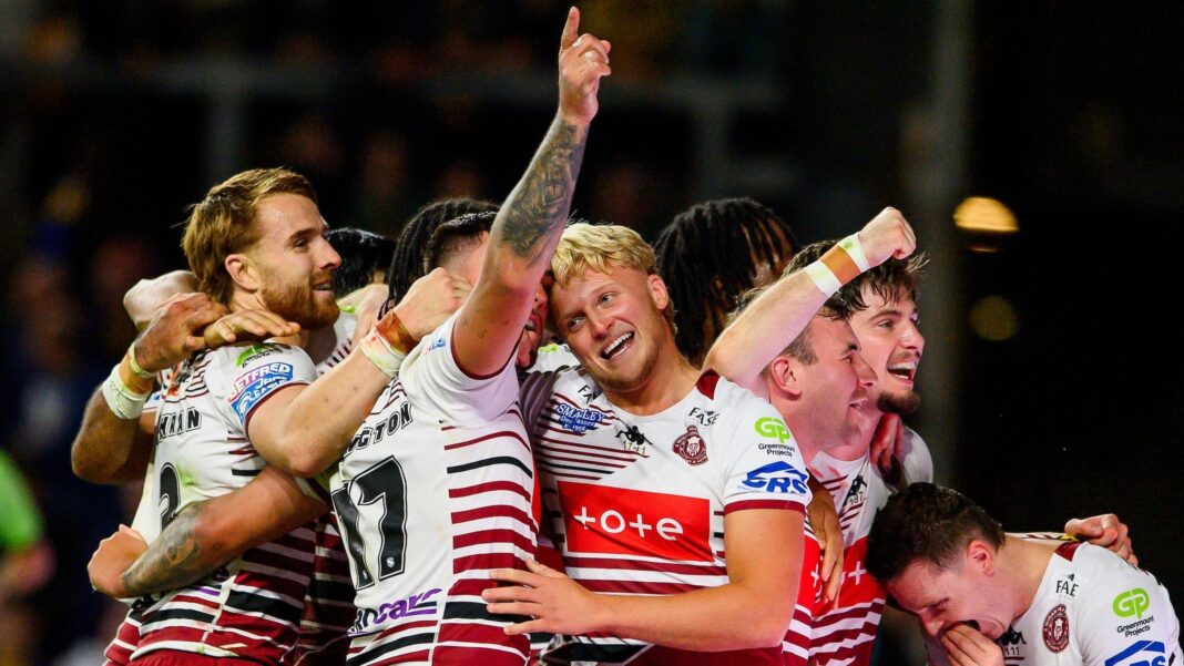 Wigan's Oliver Partington (17) has his right arm raised in celebration while being hugged by a number of team-mates after one of their seven tries against Leeds