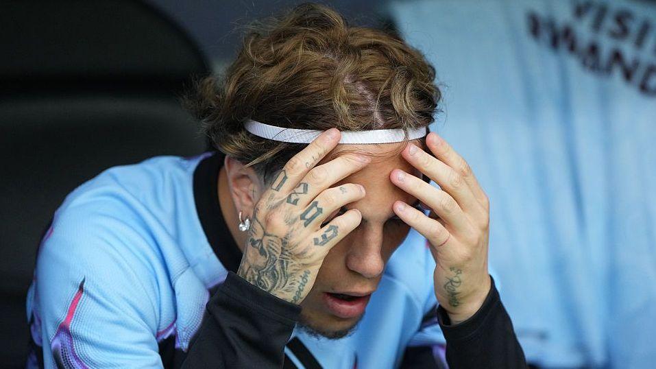 Alejandro Garnacho, wearing a light blue training top and white headband, has his tattooed hands held up to his forehead while looking downwards