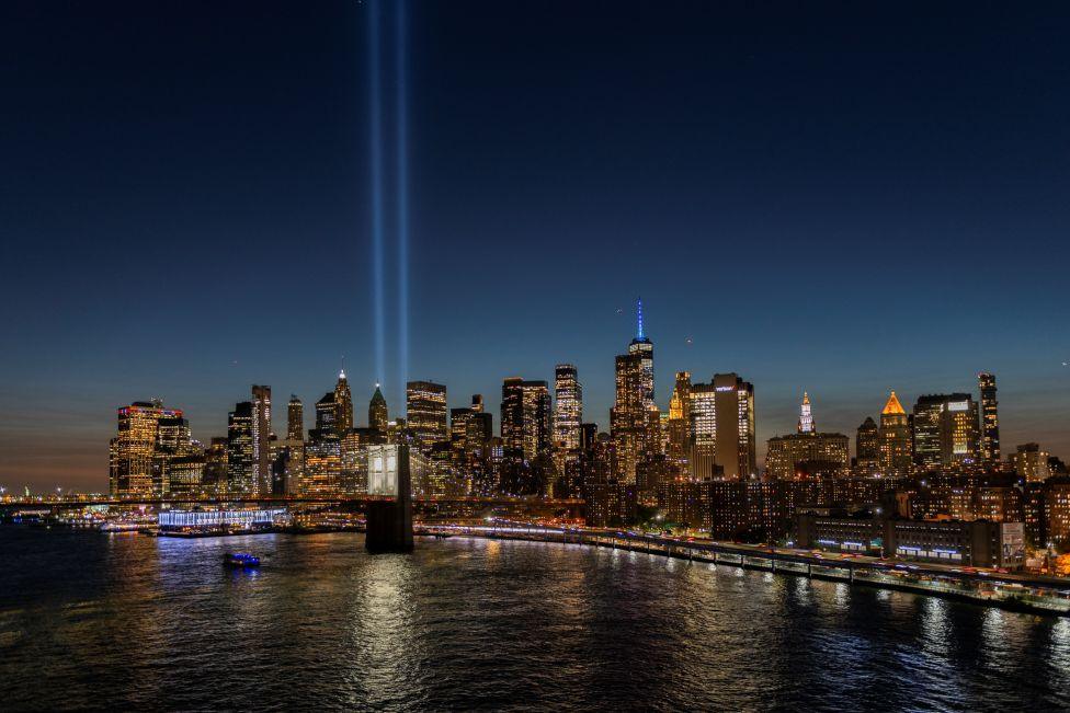 Manhattan skyline at night with the skyscrapers all lit up against a dark sky. Two beams of light are emitted from One World Trade Center to commemorate the twin towers that were destroyed in 2001