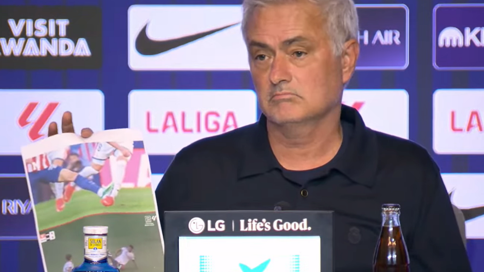 A frowning Jose Mourinho at his news conference with screenshots of incidents he believed should have brought about red cards for Atletico Madrid players. In the background is an advertising board featuring sponsor and competition logos.
