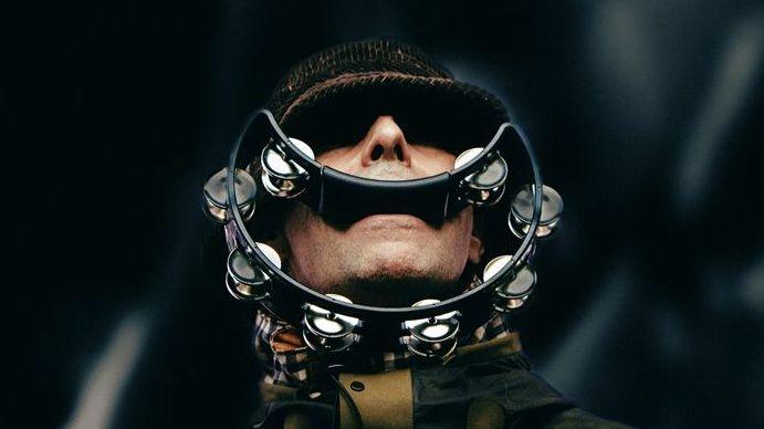 Liam Gallagher of Oasis with his eyes shaded by the peak of his hat, with a smile-shaped tambourine in his mouth