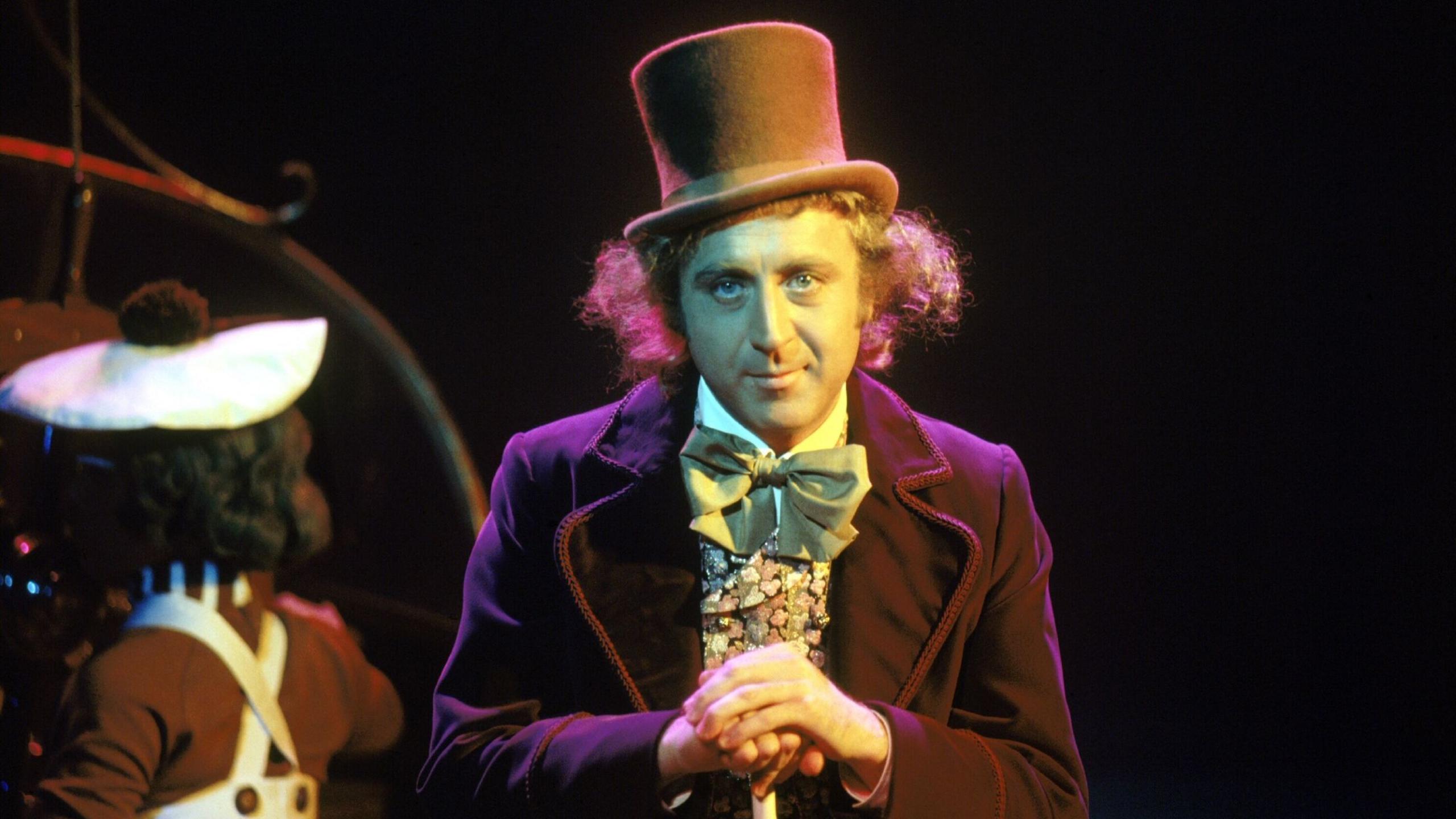 A still of Gene Wilder from Willy Wonka & the Chocolate Factory with an Oompa Loompa behind him