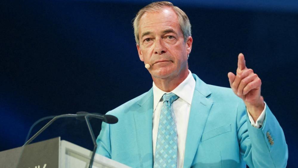 Nigel farage, wearing a light blue suit and white shirt, gestures with his left hand