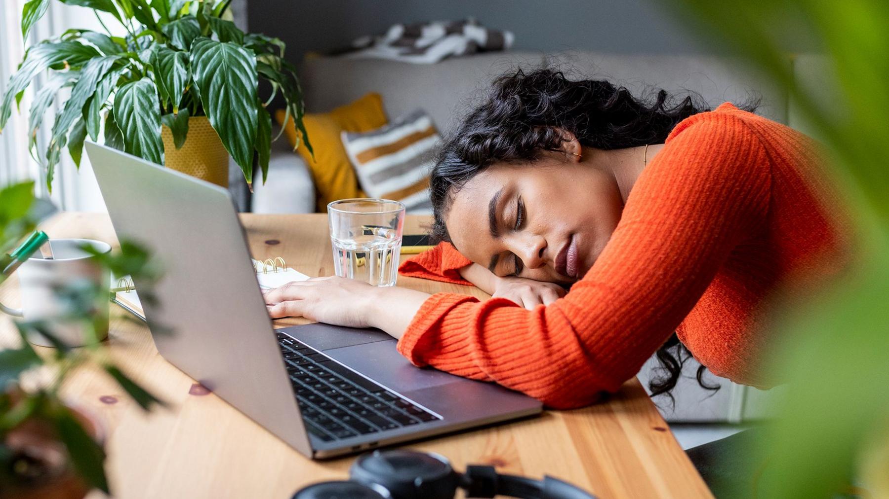 A tired young woman alspeep on her desk in front of a laptop