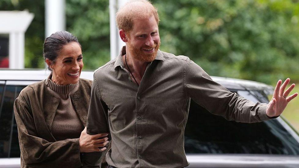 Harry and Meghan ‘surprised’ by King’s letter making clear they remain non-working royals Meghan holding onto Harry's arm, while Harry waves his hand