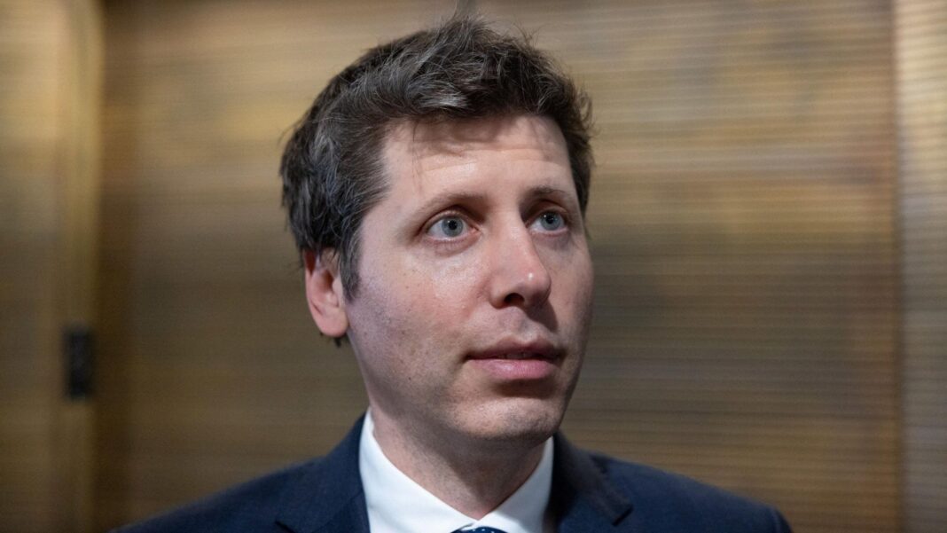 OpenAI CEO Sam Altman standing before a lobby of elevators answering questions from reporters.