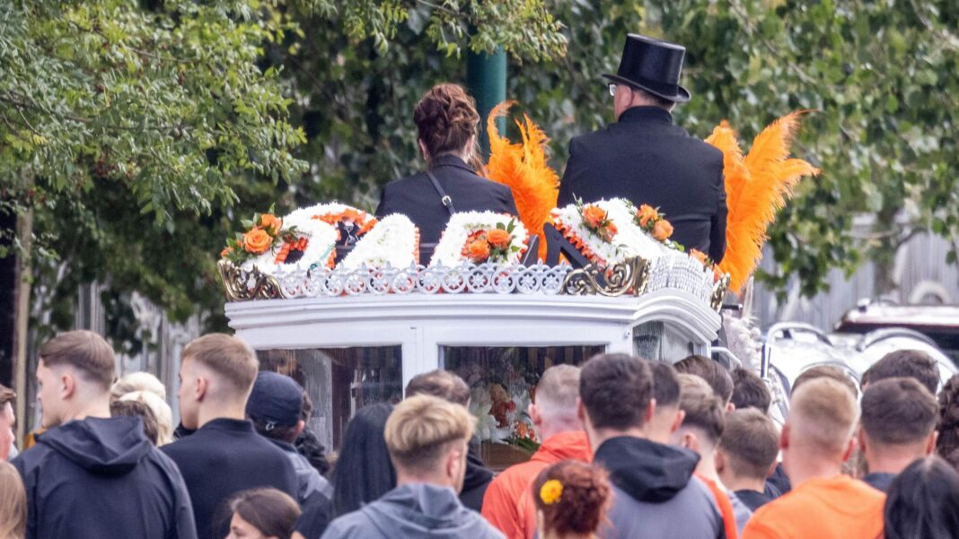 Schools close early for A66 crash funeral The white horse-drawn hearse carrying Jakub Matusiak's coffin arrives at St John's Church, Middlesbrough. Plumes of orange feathers can be seen as a crowd of people look on.