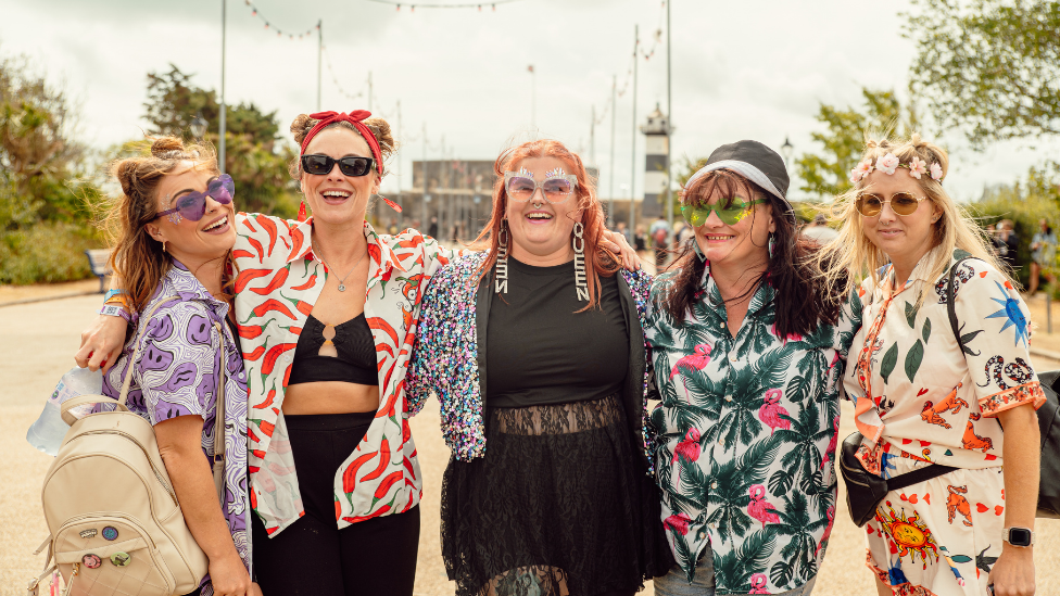 Five women dressed in festival attire stood in a line and smiling into the camera