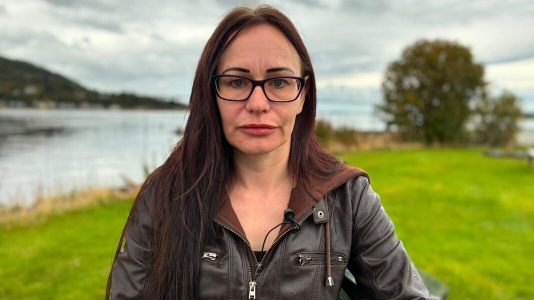 Worker at care home investigated by BBC struck off for threatening elderly man Su Christie has long dark hair and black-rimmed plastic spectacles. She is wearing a brown leather jacket and is sitting in a field by a river with the Cessock Bridge in the distance behind her.
