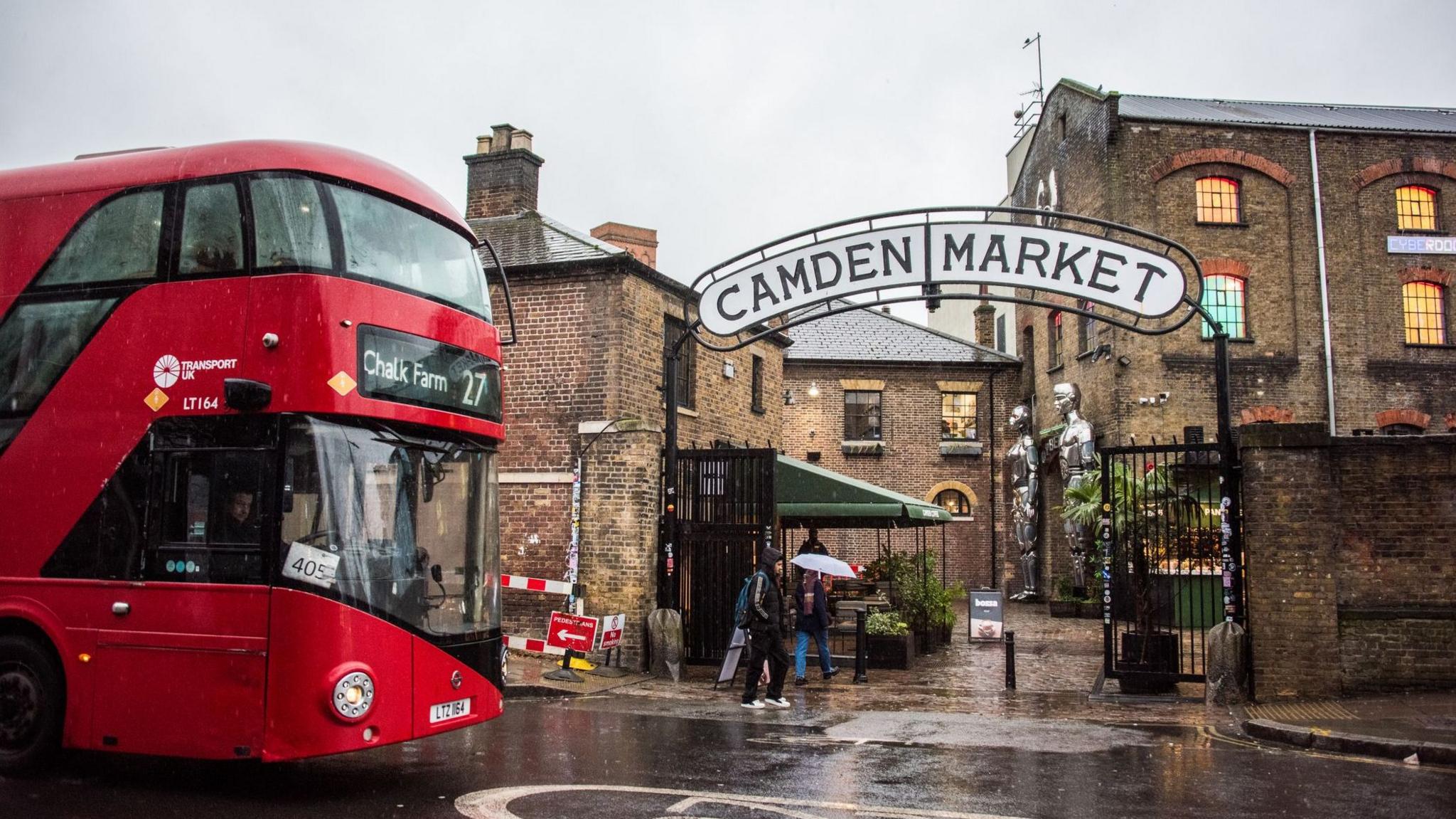 A red London bus heading to Camden Town passes by the entrance to Camden Market.