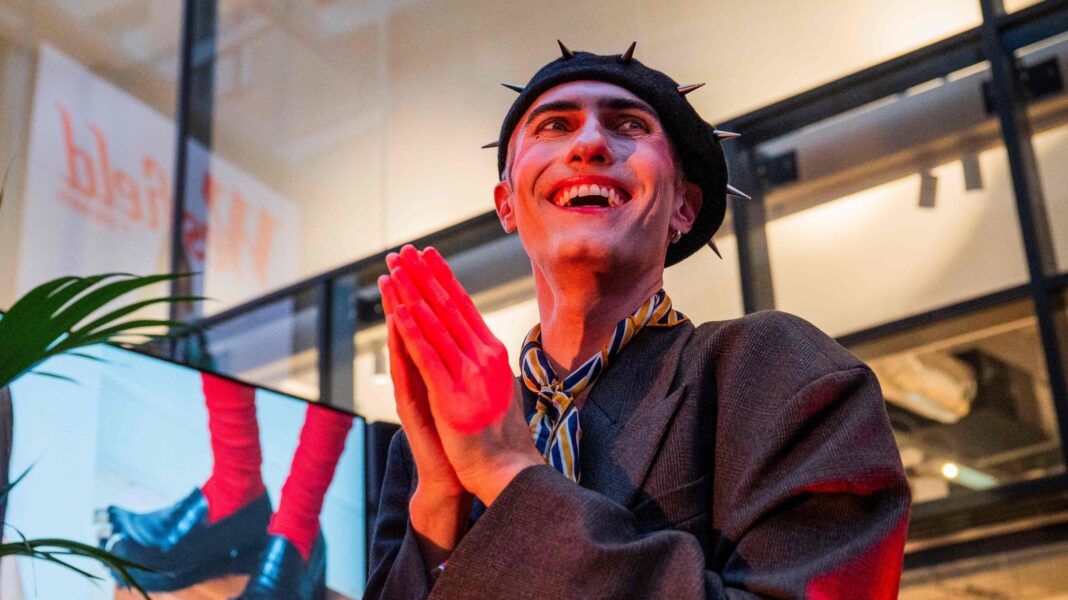 Can you take the ‘London’ out of London Fashion Week? Charles Jeffrey wears a spikey beret with a yellow and blue scarf, a large grey blazer and small hoop earrings.