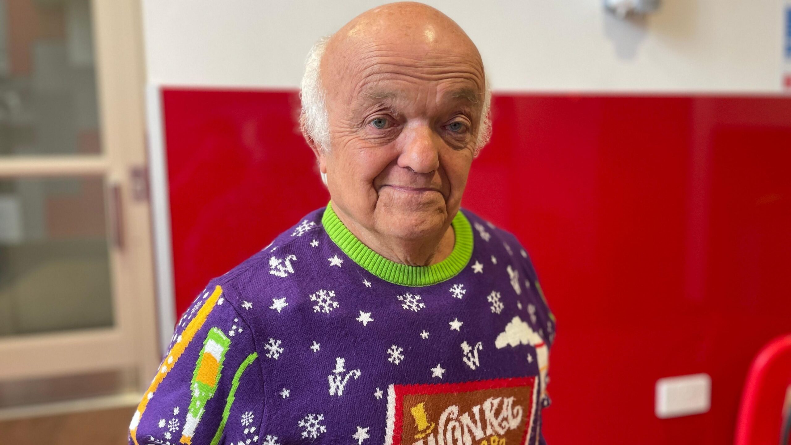 Rusty is stood with a red backdrop wearing a Wonka themed Christmas jumper