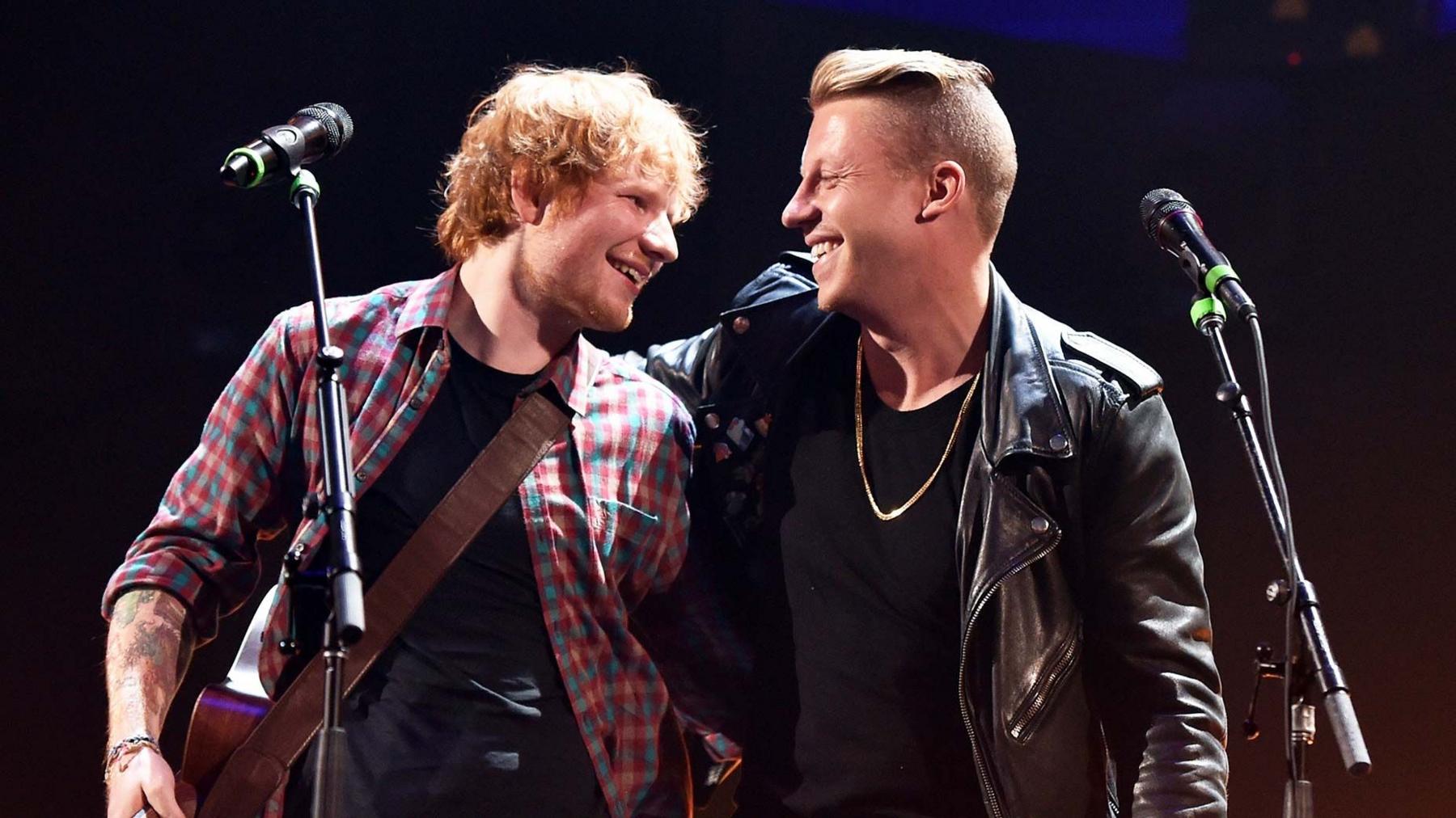 inger/songwriter Ed Sheeran (L) and rapper Macklemore perform during the 2014 iHeartRadio Music Festival at the MGM Grand Garden Arena on September 20, 2014 in Las Vegas, Nevada. Sheeran is wearing a checked shirt and holding a guitar. Macklemore is wearing a black jacket. They are smiling at each other