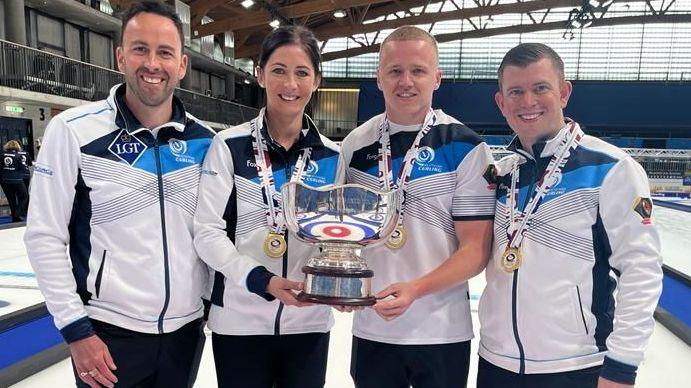 Eve Muirhead and Bobby Lammie holding the trophy after winning world mixed doubles gold in 2022