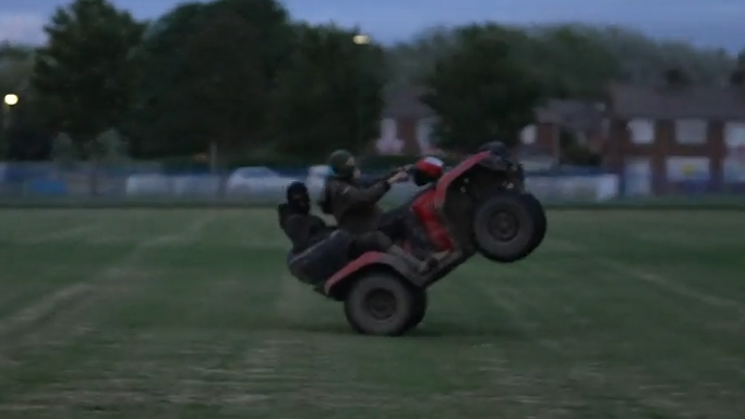 Two young men pull a wheelie on a quad bike on some grass