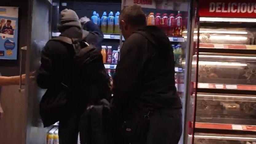 Two men dressed in black face a fridge while they fill rucksacks