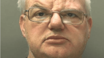 Mugshot of man with white silver hair looking at the camera. He has thin glasses that are wonky on his face
