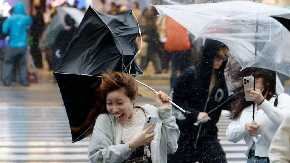 A woman holding an umbrella being blown into the wind,.