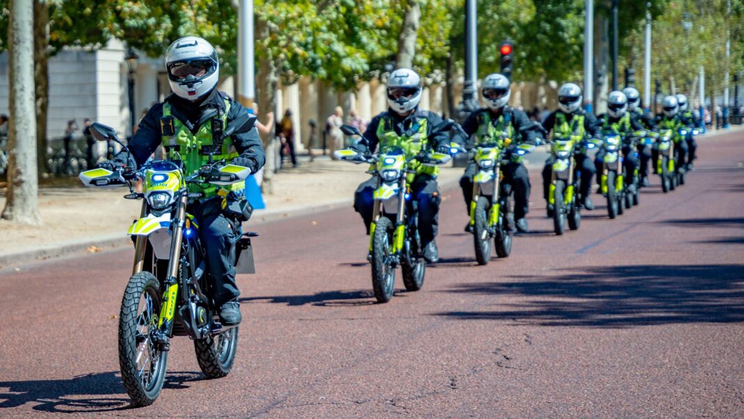 Balaclava boys on electric bikes: How to tackle the problem? A line of Metropolitan Police officers riding high-powered e-motorbikes down a paved London road in single file formation, wearing full protective gear and high-visibility jackets.