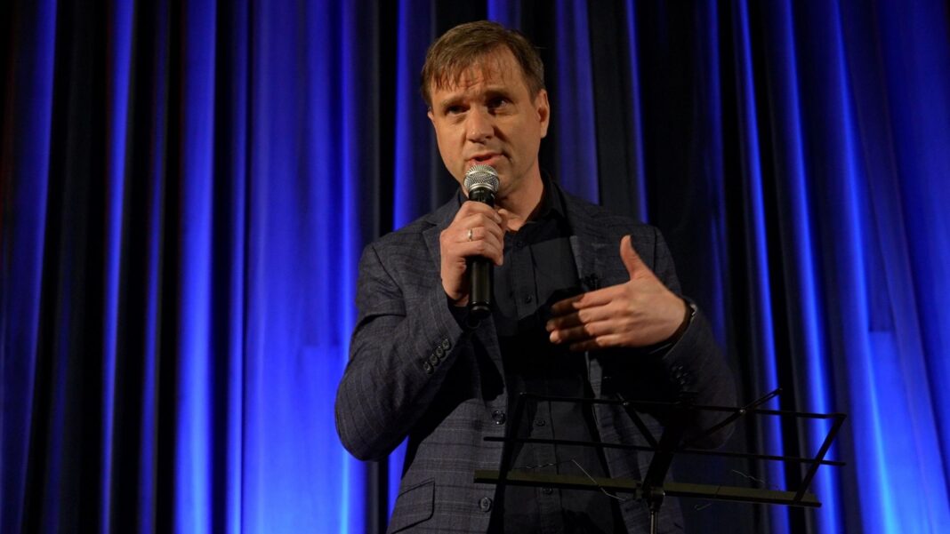 Steve Rosenberg: Russia’s elections will have few surprises, but for the Kremlin they matter Grigory Grishin delivering a speech. He holds a microphone, and is wearing a dark suit and shirt. He stands in front of a blue curtain.