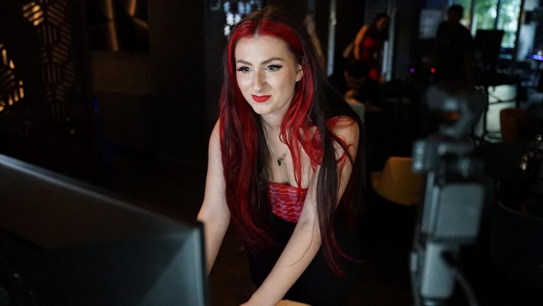 Unis are offering degrees in content creation for £30,000. But are they worth it? Knightenator, who has bright red hair, looks at her computer screen in a darkened room