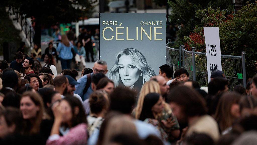 A poster with Dion's face near a crowd in Paris