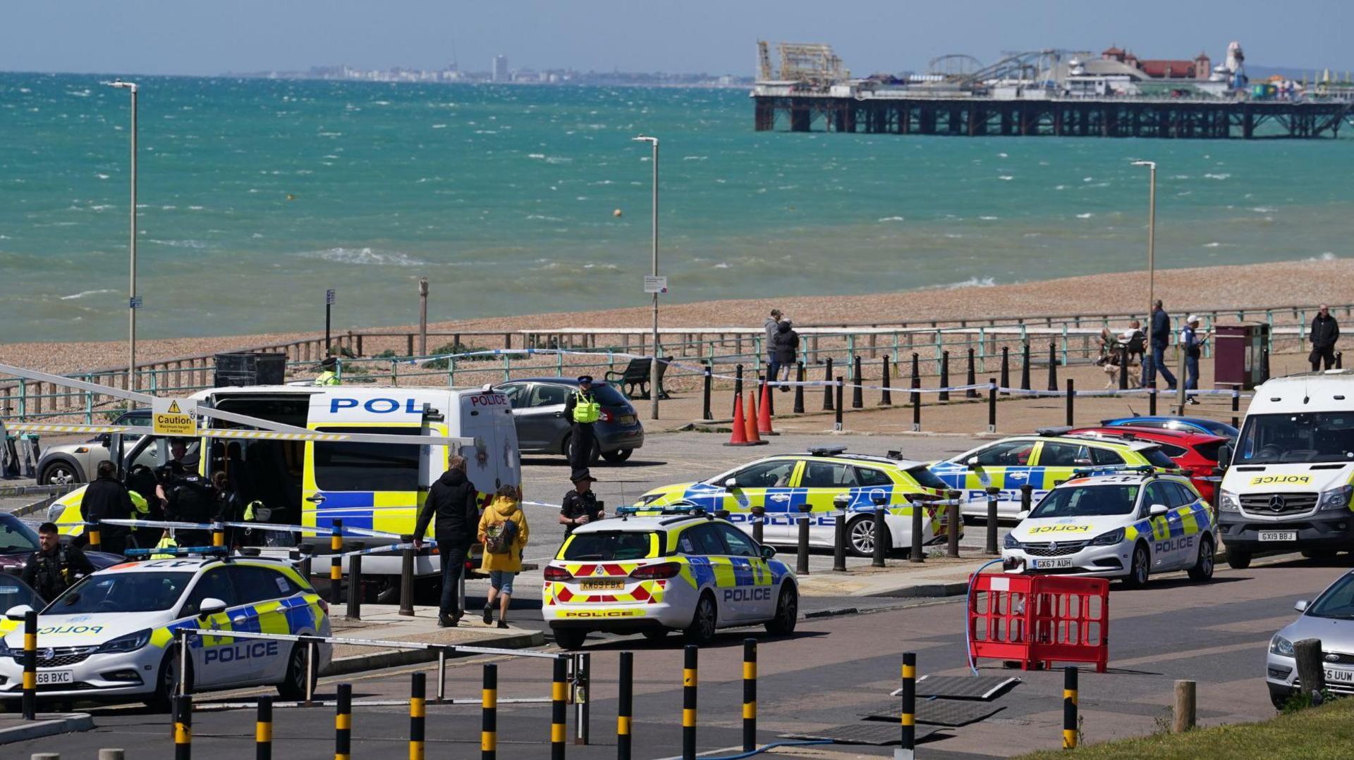 Various police vehicles in a car park on Brighton seafront. Brighton Palace Pier and a choppy sea are in the background.