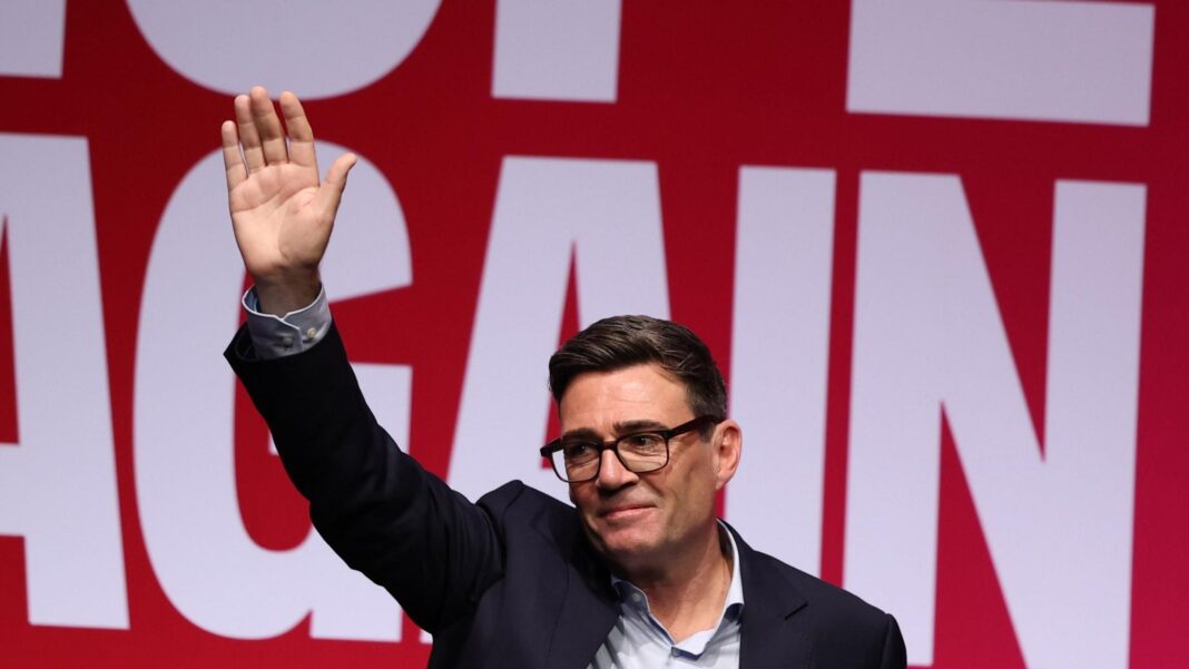 Andy Burnham waves to the audience in Liverpool against a 