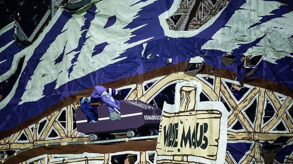 A tifo on display at VfL Osnabruck stadium, showing a rollercoaster cart on a track with dummies inside