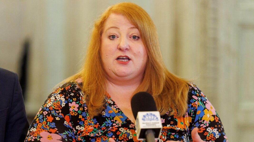 Judge explains compassionate release of murderer who failed to return to NI jail Naomi Long speaking into a microphone. She is wearing a patterned top and has long red hair.