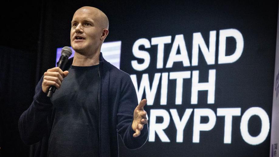 Coinbase chief executive Brian Armstrong holds a microphone while speaking at an event.