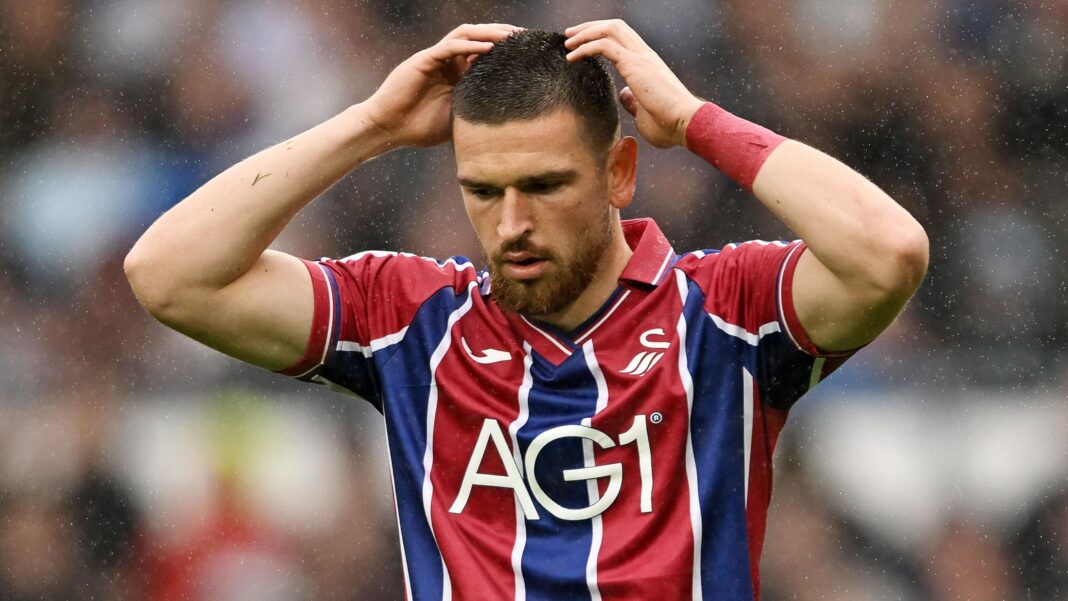 Zan Vipotnik wearing a red and blue striped Swansea away shirt with his hands on his head