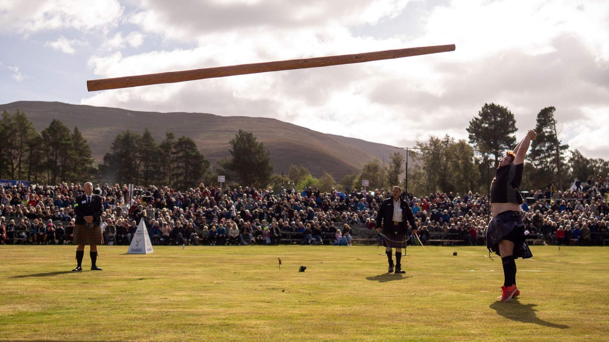 a man in a kilt and t-shit tossing a caber as spectators look on