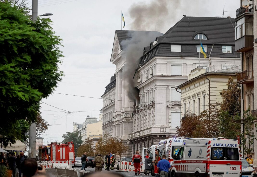 Russia hits Ukrainian security headquarters in drone attack, Zelensky says Black smoke pours from two windows in a large government building with Ukrainian flags on the facades. Ambulances and security personnel crowd the street below.