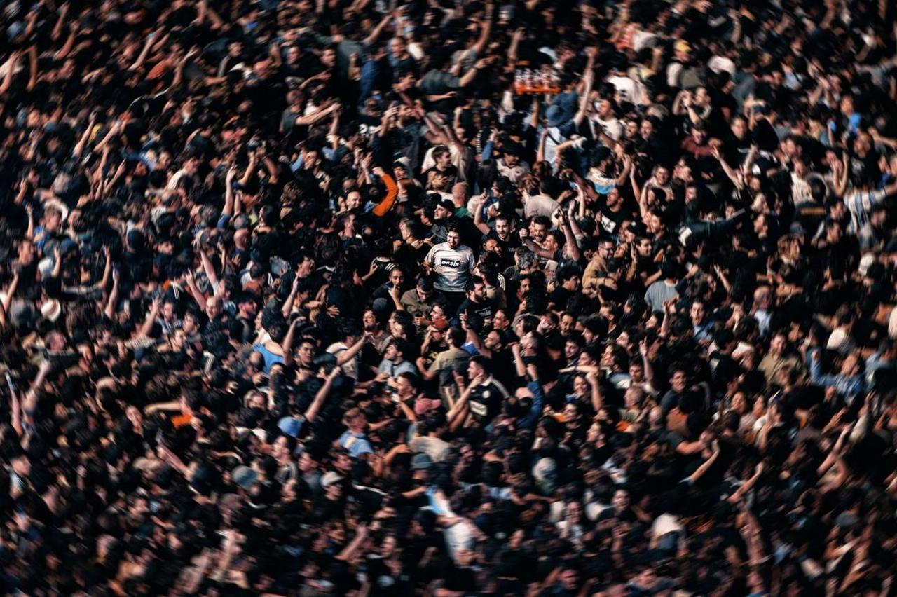 A man in a classic light blue Oasis t-shirt (centre) surveys the scene as all hell breaks loose around him during one of the band's reunion concerts