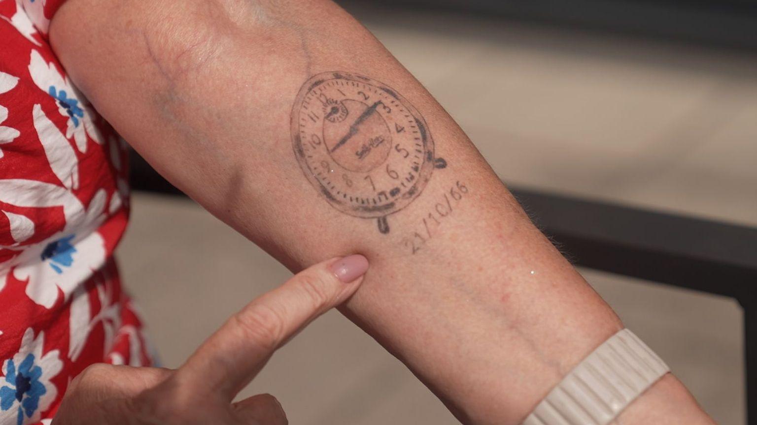 A woman points at a tattoo of a clock on her forearm