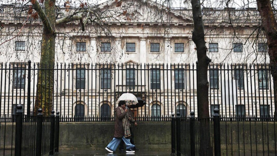 UK research funded by China front company being sent to Beijing’s spies, MI5 warns A woman holding an umbrella past black railings in front of the Royal Mint Court, the proposed site of the new Chinese embassy in London.