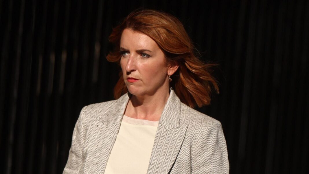 UK First Secretary of State Louise Haigh dressed in a grey blazer and white top with her red hair out and blowing as she walks.