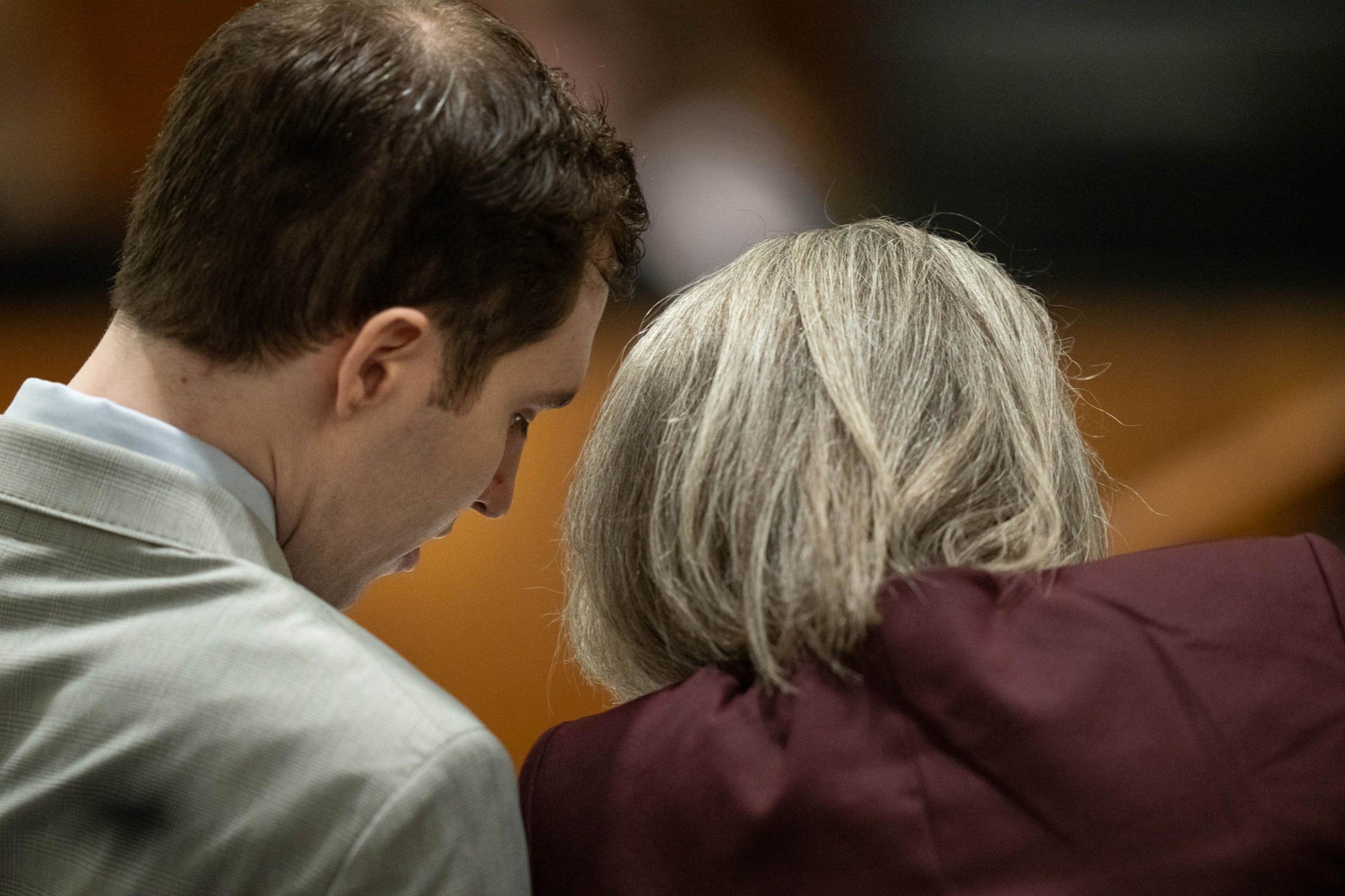 Tyler Robinson, wearing a grey suit and light-coloured shirt, leans in to consult with defence attorney Staci Visser, her blond-grey hair styled neatly to her shoulders over a maroon blazer; only the side of Robinson's face and the back of Visser's head can be seen