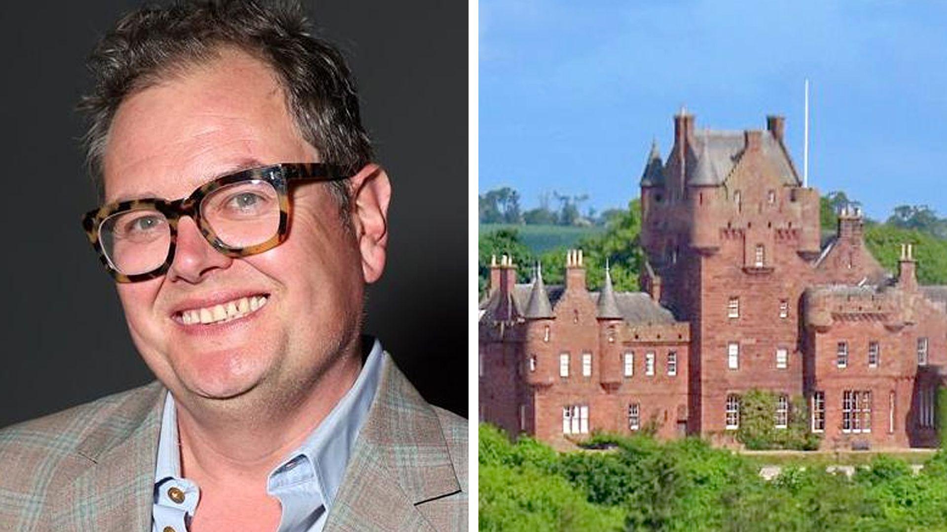 Alan Carr in a brown and light green checked suit jacket with a blue shirt underneath and brown, thick-rimmed glasses and a castle.