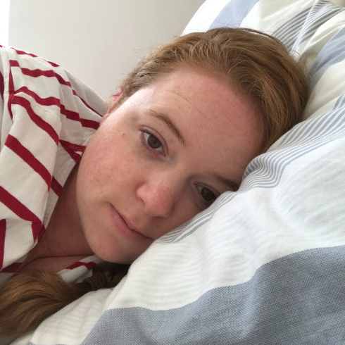 Woman with red hair lying in bed, facing the camera with a sad expression.