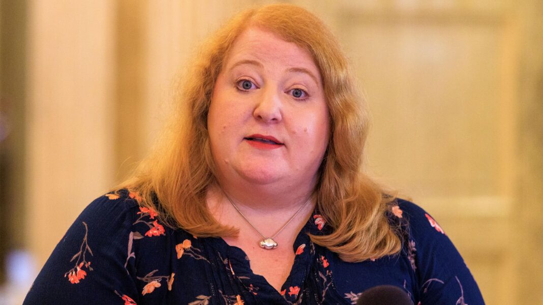 A woman with light hair, she has a navy top with pink flowers on it