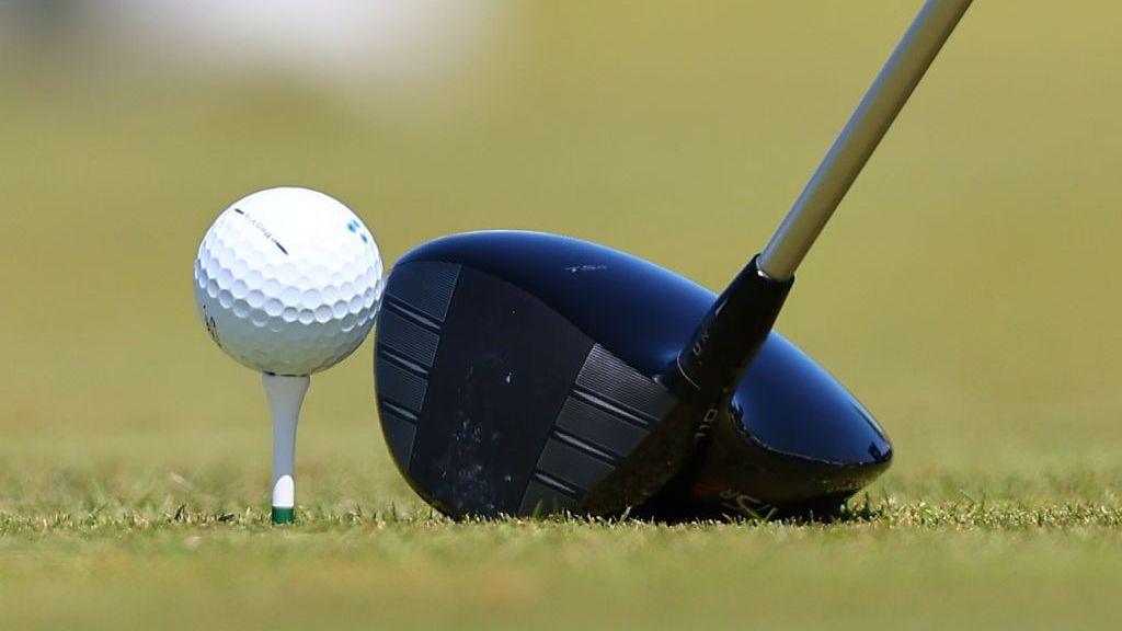 Generic shot of a golf driver next to a gold ball on a tee