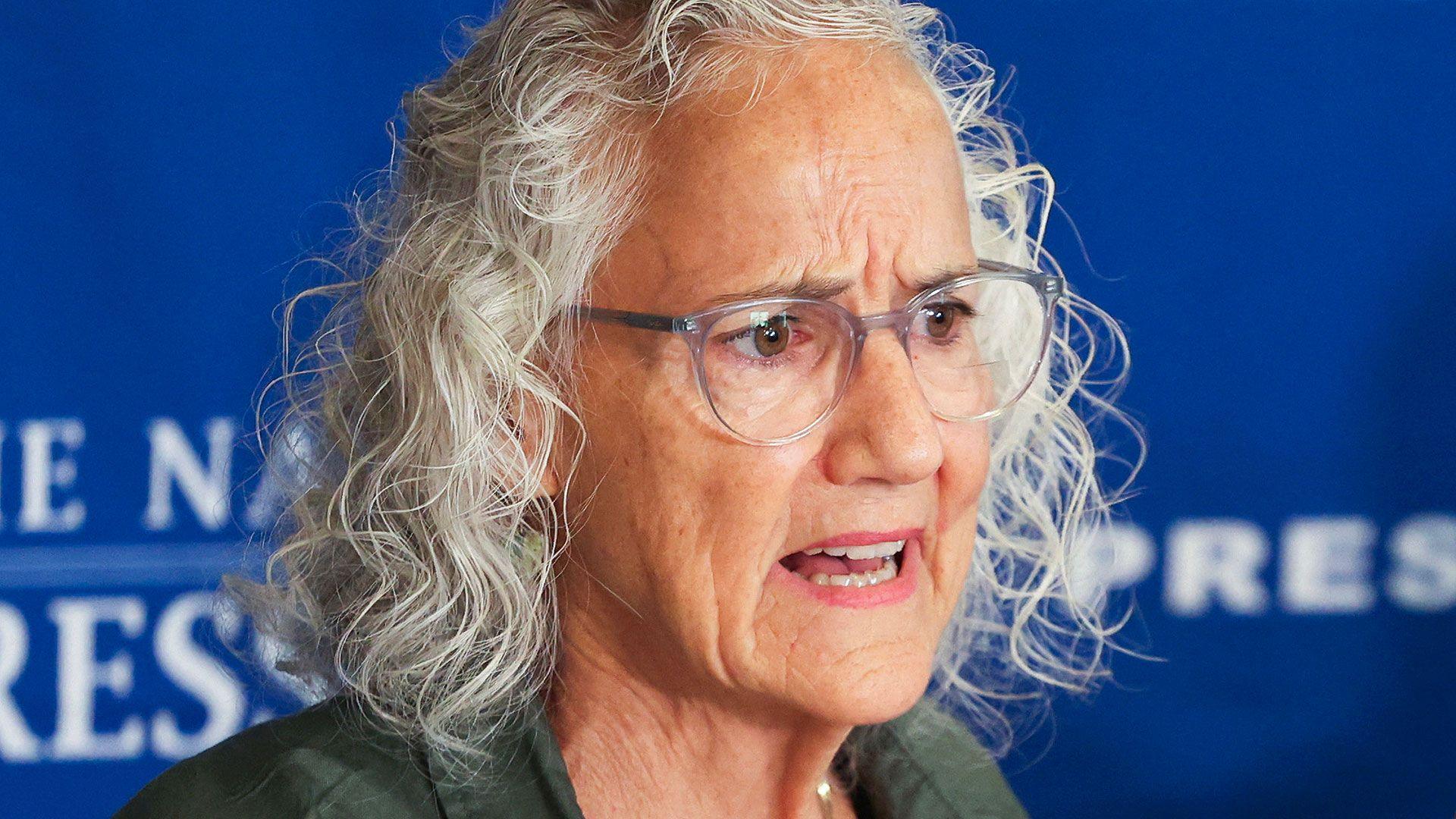 Debra Tice has grey wavy hair, brown eyes and wears glasses - pictured here at the National Press Club in Washington, DC
